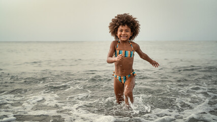 Wall Mural - Afro child having fun playing inside sea water during summer holidays - Childhood and travel vacation concept