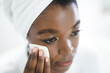 © Wavebreak Media - Smiling african american woman in bathroom cleansing her face with cotton pad for skin care