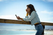 © Wavebreak Media - Mixed race woman using smartphone on sunny day by seaside