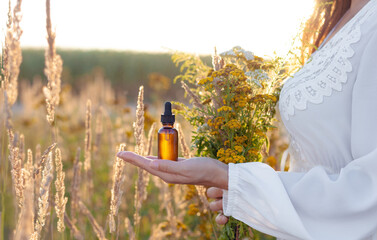 Wall Mural - A woman in a white dress holding a bottle with a dropper in the background of herbs, a field meadow. ALTERNATIVE MEDICINE