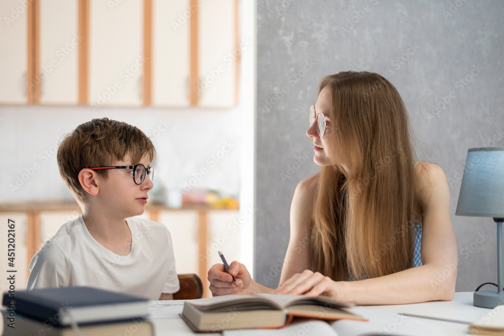 Mother explains to her son how to do his homework. Young tutor works ...