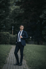 Wall Mural - Vertical shot of a young attractive man in a classic outfit on a park pathway