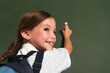 cheerful schoolkid looking away while writing on chalkboard