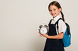 positive schoolkid holding large alarm clock while looking at camera isolated on grey