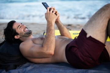 Handsome man using the phone. Surfer taking a break on the beach.