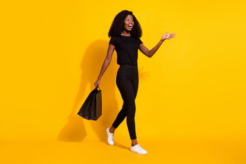 Poster - Full length photo of mad millennial young lady go wear black outfit hold bags isolated on yellow color background