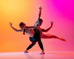 Two dancers, stylish sportive couple, male and female models dancing contemporary dance on colorful gradient yellow pink background in neon light.