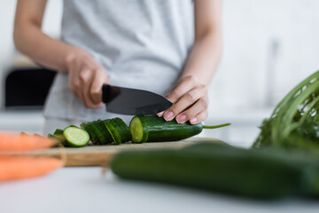 Wall Mural - partial view of woman cutting fresh cucumber on blurred foreground.