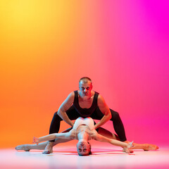 Art performance. Two dancers, stylish sportive couple, male and female models dancing contemporary dance on colorful gradient yellow pink background in neon light.