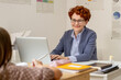 © pressmaster - Contemporary young teacher looking at schoolgirl while using laptop at lesson