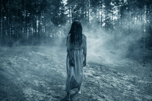 Girl In Image Of Scary Zombie Walks In Dark Forest Among Smoke.