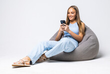 Laughing Young Woman Sitting On Beanbag Chair For Living Room And Use Phone Isolated On White Background