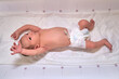 A newborn baby in diapers on a white changing table with a ruler with a Moro reflex