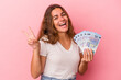 © Asier - Young caucasian woman holding bills isolated on pink background  joyful and carefree showing a peace symbol with fingers.