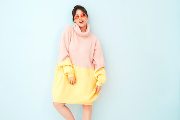 Wall Mural - Young beautiful smiling female in trendy summer colorful sweater. Sexy carefree woman posing near pink wall in studio. Positive model having fun indoors. Pretty and cheerful