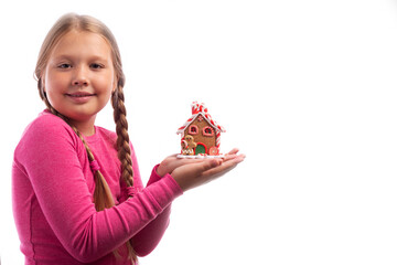 Little girl with blond hair holding a gingerbread house in her hands on a white background