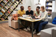 © Seventyfour - Full length view at diverse group of young people studying together at table in college library, copy space