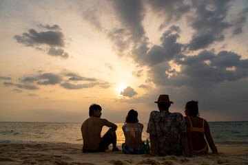 Wall Mural - Group of Happy Asian man and woman friends sitting on the beach enjoy drinking beer with talking together at summer sunset. Male and female friendship relax and having fun outdoor lifestyle activity.