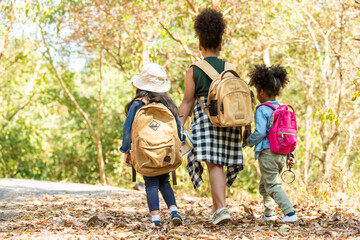 Group of Diversity little girl friends with backpack hiking together at forest mountain in summer sunny day. Three kids having fun outdoor activity sitting and looking at the map exploring the forest.