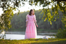 Beautiful Girl In A Vintage Rose Dress Walks By The Lake With A White Fluffy Rabbit