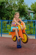 Teen girl sits on toy motorbike on playground