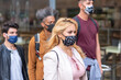 © MandriaPix - multiethnic urban crowd of young people walking the streets, wearing a facemask, focus on the sad and worried look of a blonde woman, social distancing, the new normal way of living the city