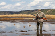 a hunter makes a placement of duck decoy on a muddy lake