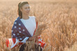 Woman with American flag and with a sheaf of ears in wheat field at sunset. 4th of July. Independence Day patriotic holiday