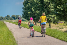 A Father, Mother And Daughter Are Cycling On A Dutch Dike. The Little Girl Is Wearing A Pink Bicycle Helmet. It Is A Sunny Day In Summertime. The Photo Was Taken In The Province Of North Brabant.
