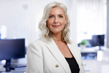 Wall Mural - Portrait of beautiful grey haired senior businesswoman standing at the office while looking at camera and smiling. 