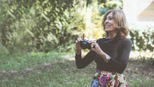 Senior Active Woman Taking Photos With A Digital Camera, In A Park In Autumn. Active Seniors Concept
