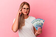 © Asier - Young russian woman holding bills isolated on pink background pointing temple with finger, thinking, focused on a task.