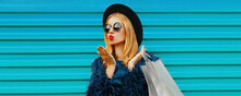 Fashionable Portrait Of Stylish Blonde Woman With Shopping Bags Wearing A Blue Faux Fur Coat, Black Round Hat On Colorful Background