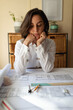 © Wavebreak Media - Caucasian female architect in living room, sitting at table working with plans