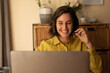 © Wavebreak Media - Smiling caucasian woman in living room, sitting at table working, using laptop wearing headset