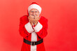 © khosrork - Portrait of elderly man with gray beard wearing santa claus costume biting nails, being nervous terrified, feeling frightened, anxiety disorder. Indoor studio shot isolated on red background.