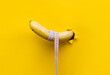 A banana with a tape measure wrapped around it appears through a torn hole in yellow paper. The concept of healthy food, diet and potency. Copy space.