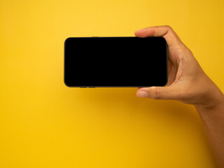 Wall Mural - hand holding of a smartphone with a yellow background. close-up photo. space for text. technology an