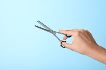 Wall Mural - Hairdresser holding professional thinning scissors on turquoise background, closeup. Haircut tool