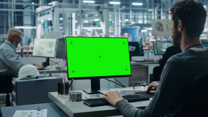 Leinwandbilder - Car Factory Office: Caucasian Male Automotive Engineer Sitting at His Desk Working on Green Screen Chroma Key Computer. Automated Robot Arm Assembly Line Manufacturing. Over Shoulder Medium Shot