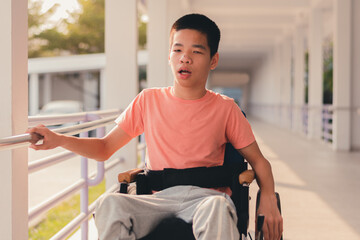 Confident handicapped teenager boy on wheelchair with happy face on walk way in hospital, Smart disabled kid activity to see a doctor and push wheel by himself,Mental health of diverse people concept.