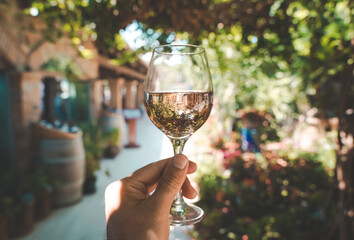 Glass of wine in hand. A glass of young fresh rose wine against the backdrop of a summer cafe in a Mediterranean seaside tourist town in the summer under sunlight. Summer, travel, lifestyle