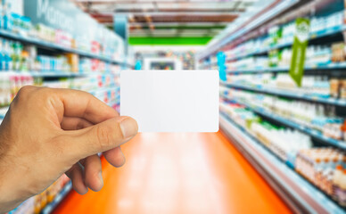 Empty plastic grocery card in hand on supermarket background. Grocery card for discounts and promotions in shops and supermarkets