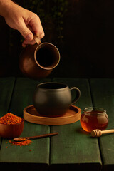 Canvas Print - Vertical shot of a hand pouring something into a mug with a honey jar near it