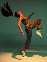 Wall Mural - Dancing athletic mixed race girl performing expressive fiery hip hop or ethnic modern dance in colourful studio light