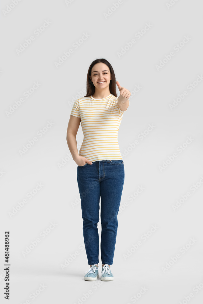 Beautiful young woman showing thumb-up on grey background