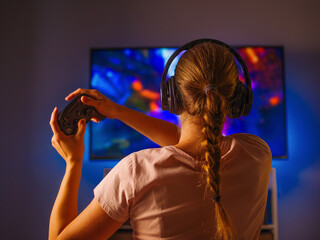 Wall Mural - A blonde girl with a joystick and headphones is playing a video game. Gamer girl. Close-up. Shooting from the back. Hobby, passion, game strategy, free time, day off.