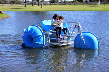 Two young girls  riding on a big wheel aqua bike water tricycle