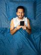 © Narayan - latin man using cell phone on blue bed, cell phone concept
