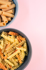 Canvas Print - Vertical shot of tri-color rotini and rigatoni pasta on a bowl isolated on pink background